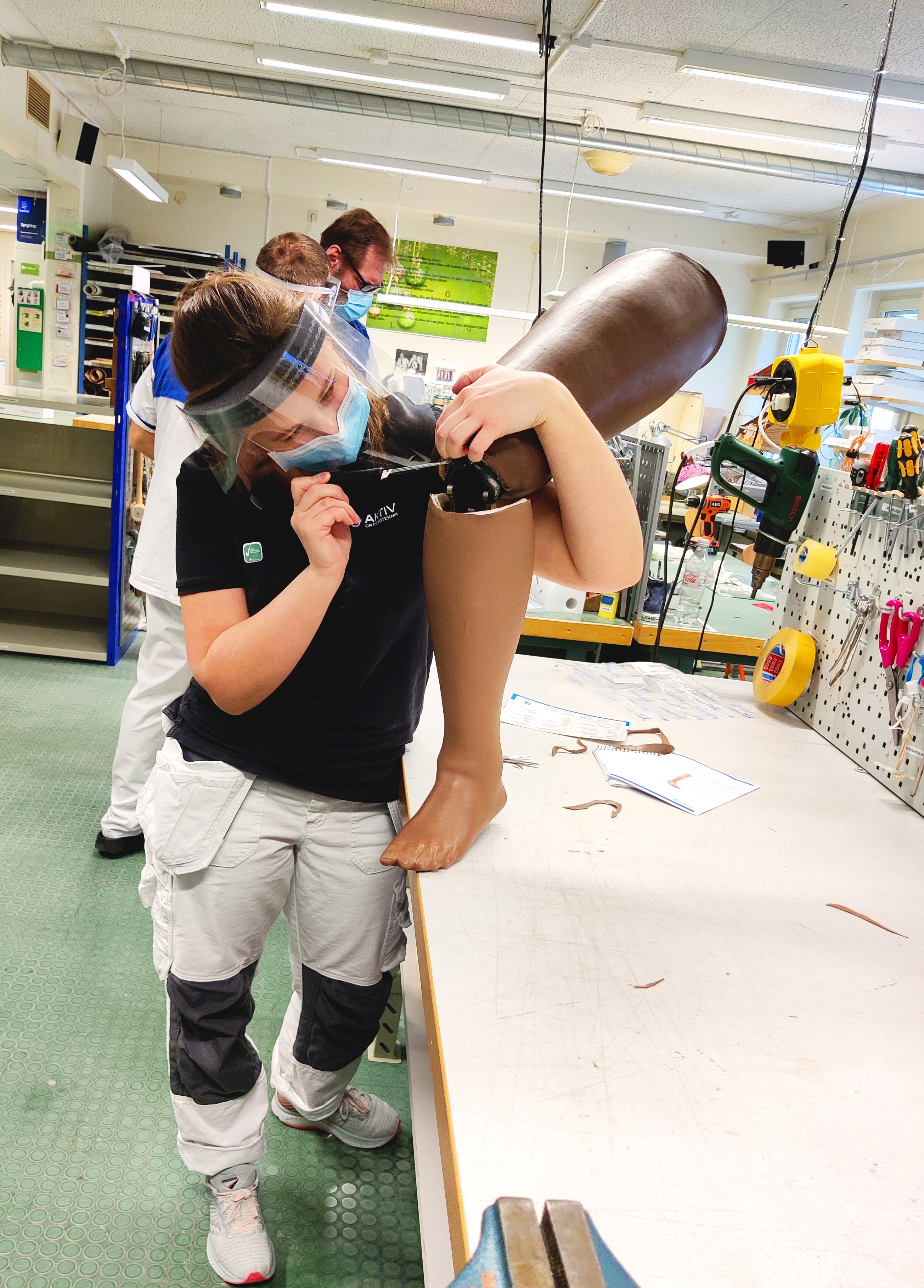 Woman with visir and face mask working on a knee prothesis in a workshop environment