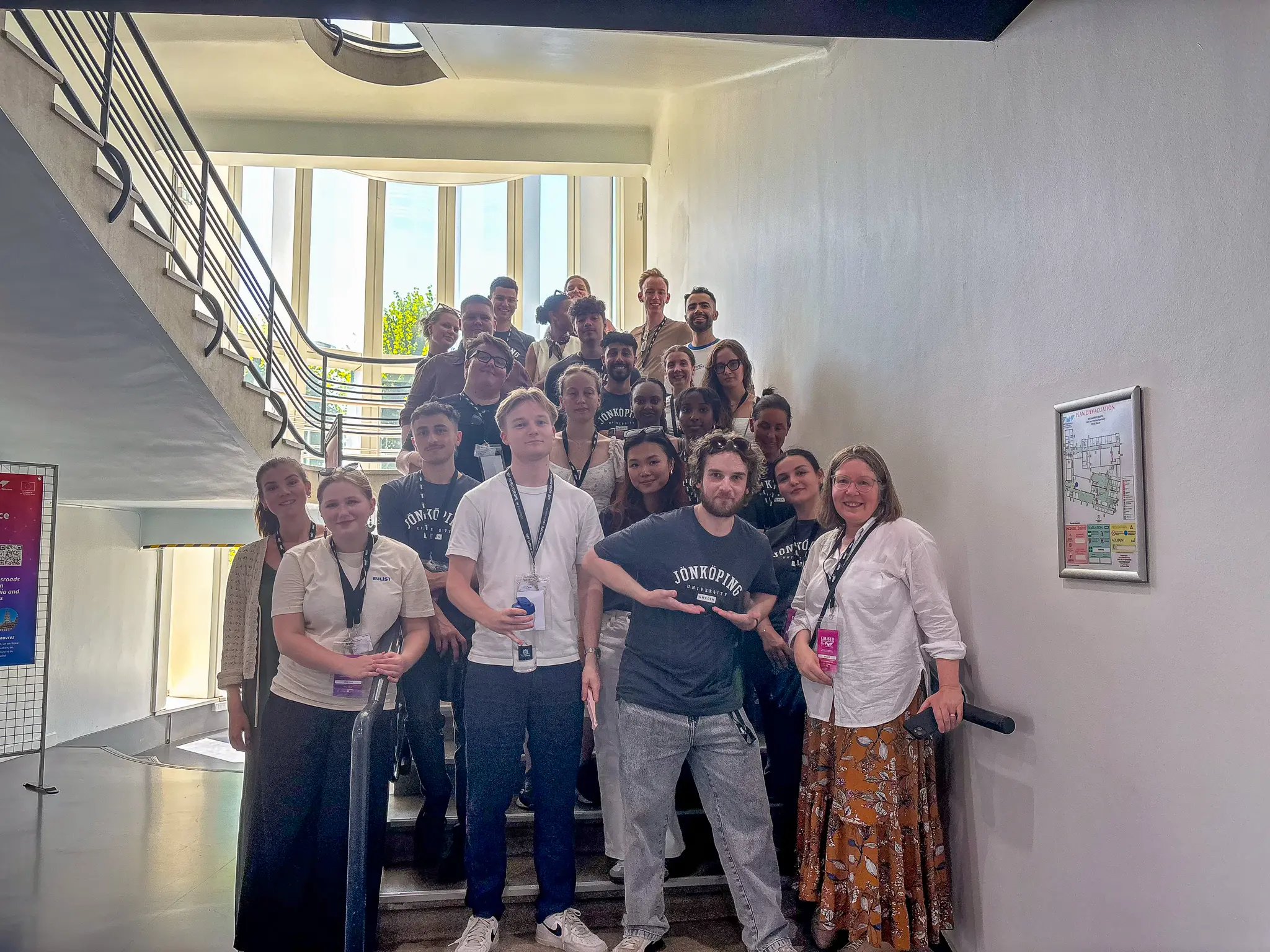 About 20 people smile and look into the camera as they stand in a stairwell