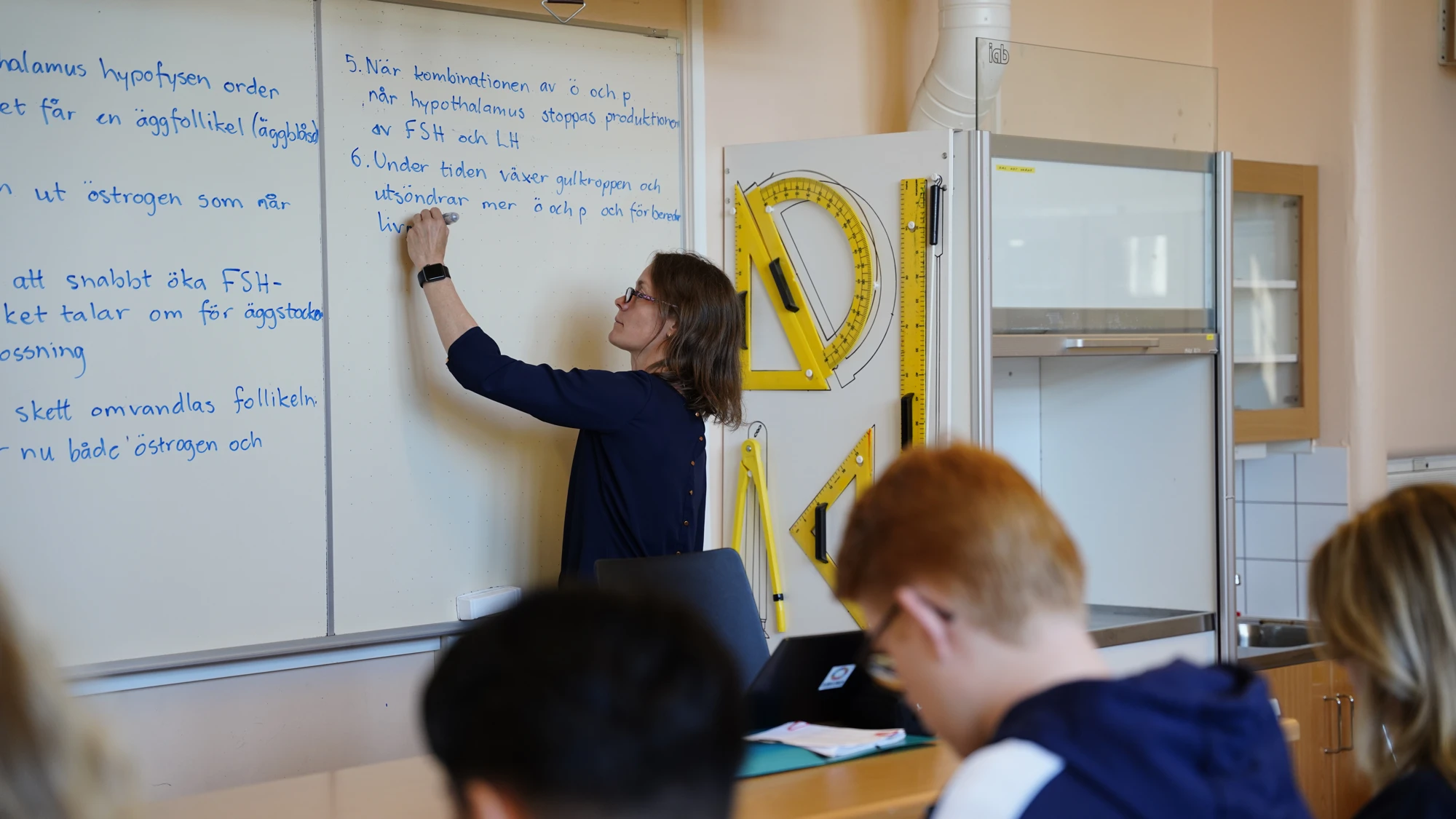 En kvinna skriver på en whiteboard i ett klassrum.