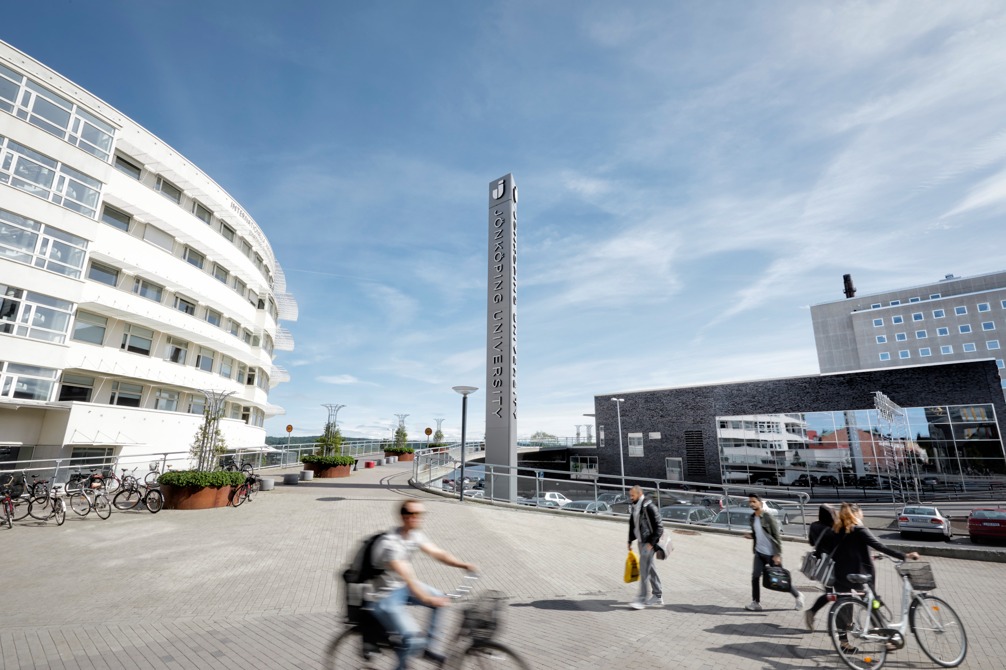 Exteriörbild på campus i Jönköping där personer med cyklar syns i förgrunden och flera av högskolans byggnader syns i bakgrunden.