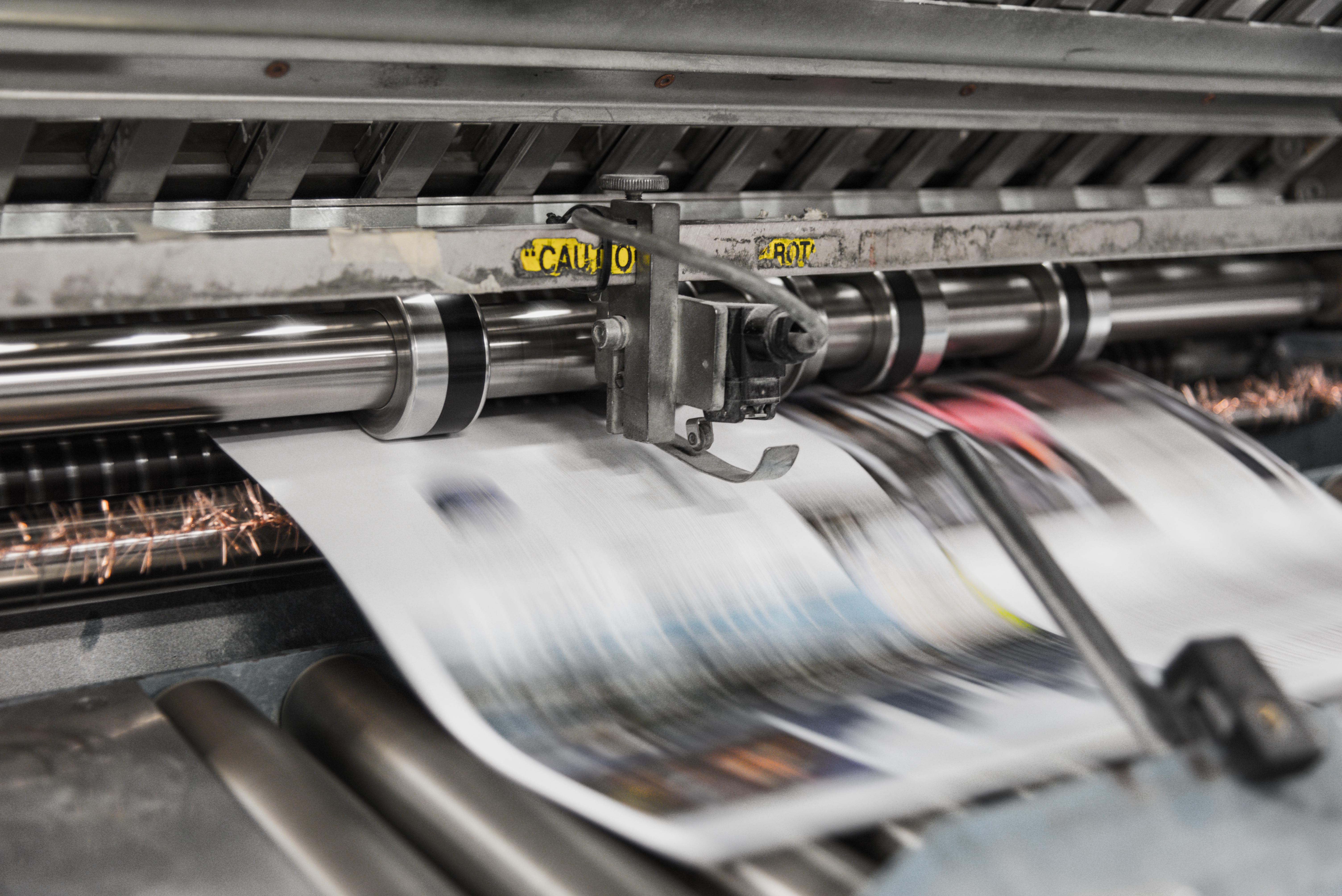 Close up of newspaper printing press with newspaper sheet coming out from under a printing roller. (image:unsplash)