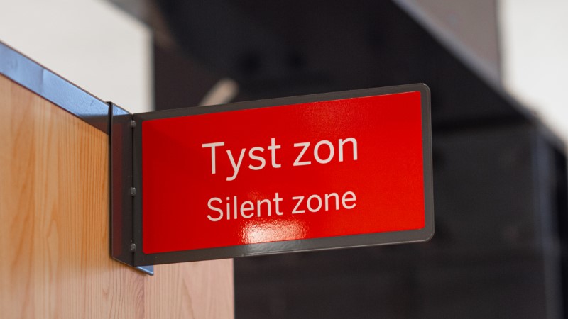 En röd skylt som hänger på sidan av en bokhylla med texten "Tyst zon"