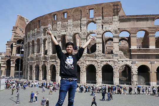 Man reaching his arms up in the air in front of the Colosseum 